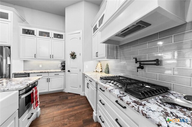 kitchen with backsplash, premium range hood, stainless steel appliances, dark wood-type flooring, and white cabinetry