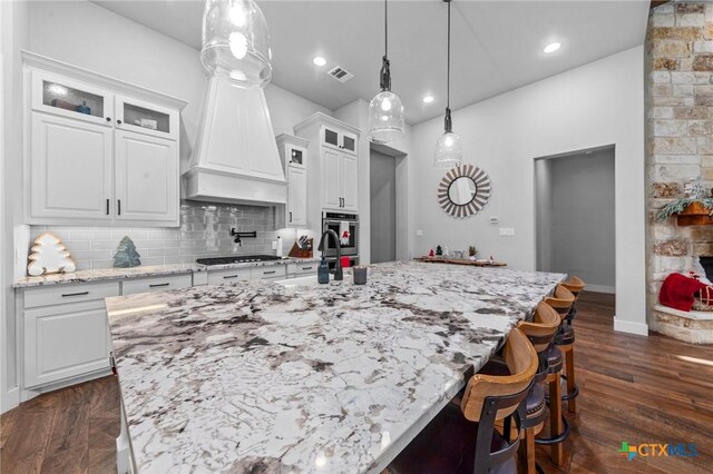 kitchen with a large island with sink, decorative light fixtures, white cabinetry, and dark wood-type flooring