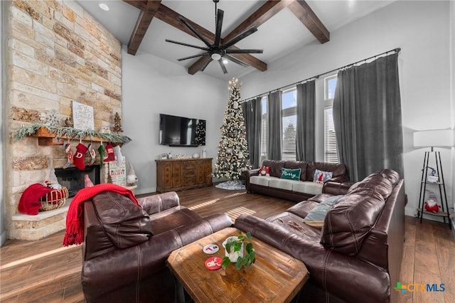 living room with a stone fireplace, beamed ceiling, and dark hardwood / wood-style floors