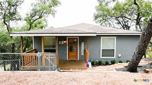 view of front facade featuring covered porch, roof with shingles, and fence