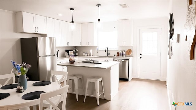 kitchen featuring decorative light fixtures, stainless steel appliances, white cabinets, a kitchen island, and a sink