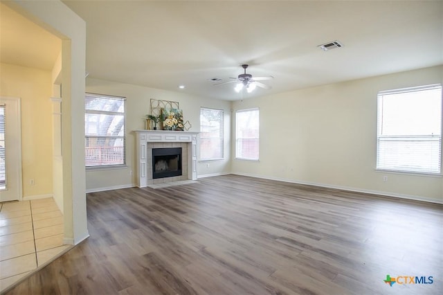 unfurnished living room featuring ceiling fan, wood-type flooring, and a tiled fireplace