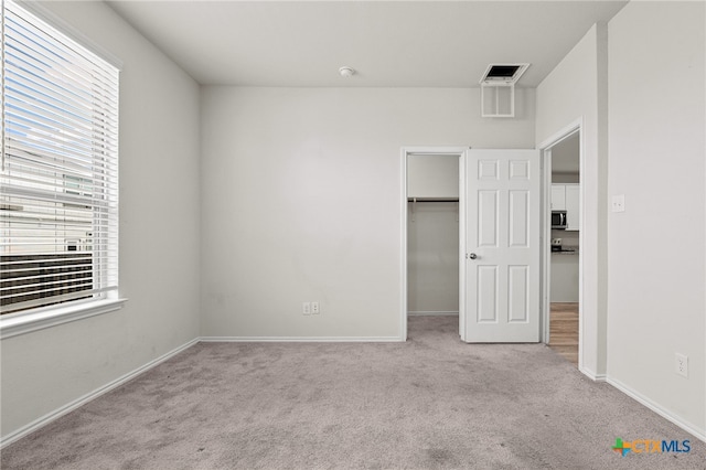 unfurnished bedroom with a spacious closet, light carpet, multiple windows, and a closet