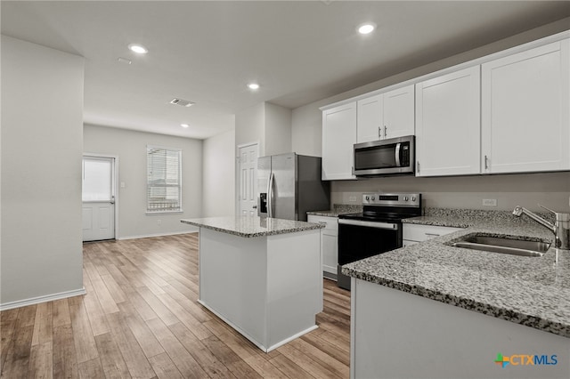 kitchen with sink, light stone counters, appliances with stainless steel finishes, and a center island