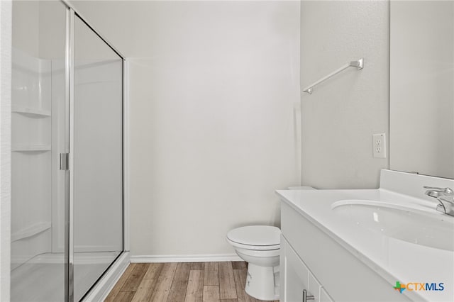 bathroom with toilet, vanity, wood-type flooring, and a shower with door