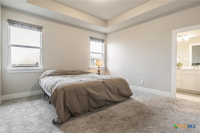 bedroom featuring connected bathroom, light carpet, and a tray ceiling