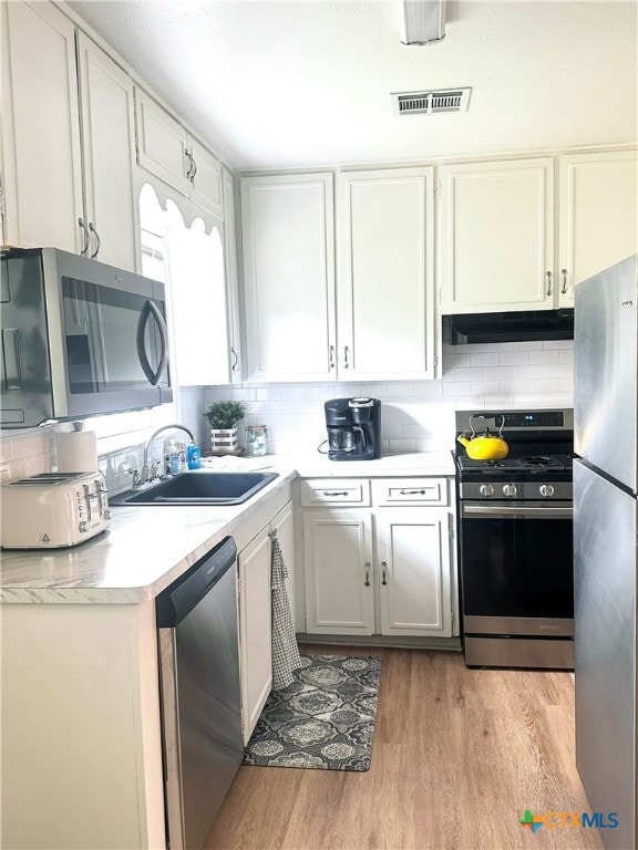 kitchen featuring stainless steel appliances, a sink, under cabinet range hood, light wood-type flooring, and light countertops