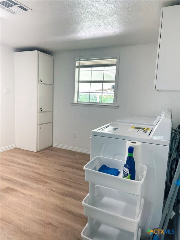 laundry area featuring washing machine and clothes dryer, light wood-type flooring, a textured ceiling, and baseboards