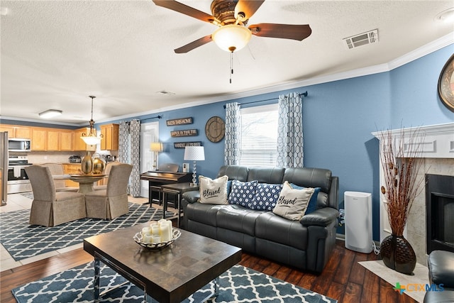 living room with visible vents, hardwood / wood-style flooring, a premium fireplace, ornamental molding, and a textured ceiling