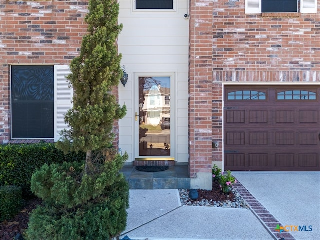 doorway to property featuring a garage and brick siding