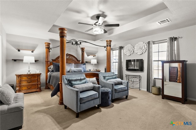 bedroom with light colored carpet, a raised ceiling, visible vents, and multiple windows