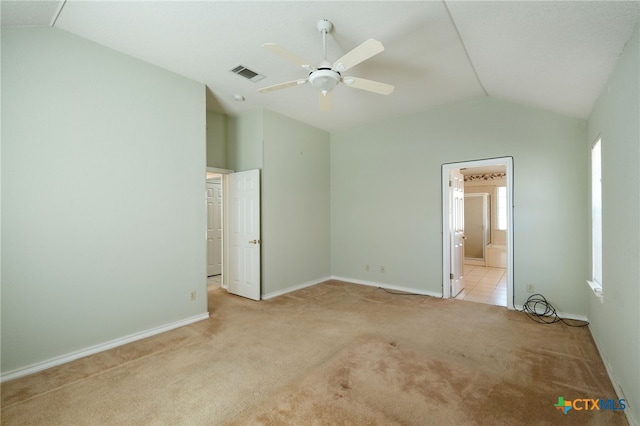 unfurnished bedroom featuring ceiling fan, ensuite bath, light colored carpet, vaulted ceiling, and multiple windows