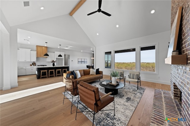 living room featuring a brick fireplace, ceiling fan, beam ceiling, high vaulted ceiling, and light hardwood / wood-style floors