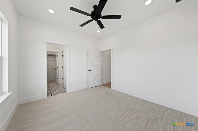 unfurnished bedroom with a walk in closet, light carpet, a closet, and ceiling fan