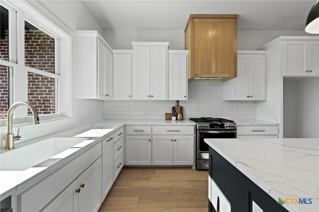 kitchen with backsplash, gas range, sink, light hardwood / wood-style flooring, and white cabinetry