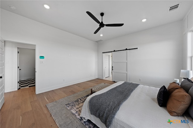 bedroom with a barn door, light hardwood / wood-style floors, and ceiling fan