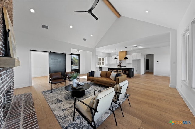 living room featuring light wood-type flooring, ceiling fan, a barn door, high vaulted ceiling, and beamed ceiling