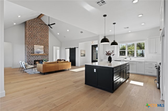 kitchen with white cabinetry, a barn door, decorative light fixtures, a kitchen island, and light wood-type flooring