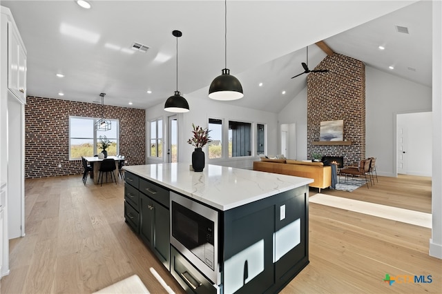 kitchen with stainless steel microwave, a center island, hanging light fixtures, brick wall, and a fireplace