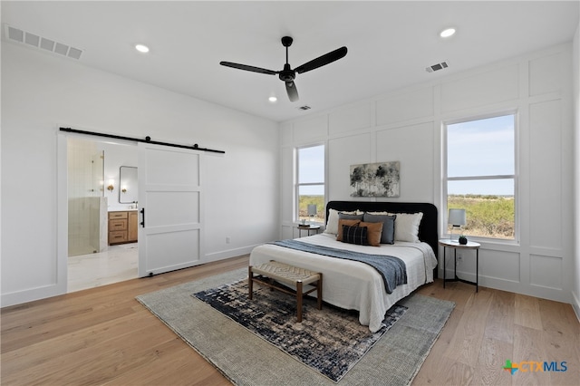 bedroom with ceiling fan, a barn door, multiple windows, connected bathroom, and light hardwood / wood-style floors