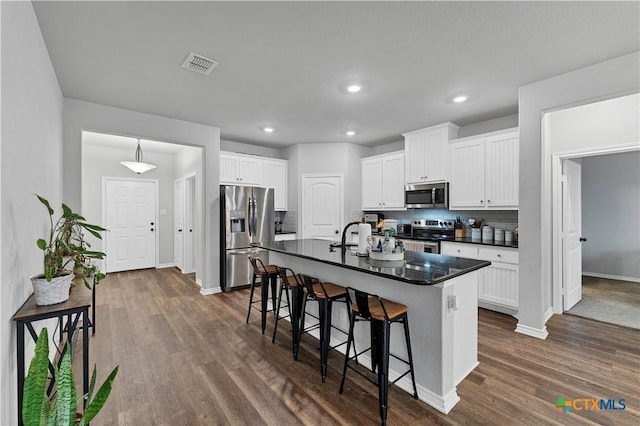 kitchen featuring a breakfast bar area, a kitchen island with sink, stainless steel appliances, white cabinets, and dark hardwood / wood-style flooring