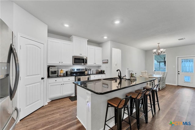 kitchen featuring a kitchen island with sink, white cabinetry, stainless steel appliances, and a kitchen bar