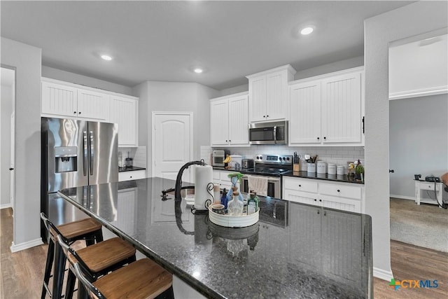 kitchen with stainless steel appliances, white cabinetry, hardwood / wood-style floors, and a kitchen bar