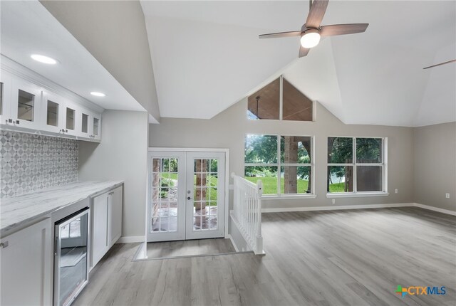 unfurnished living room featuring ceiling fan, french doors, beverage cooler, light hardwood / wood-style flooring, and vaulted ceiling