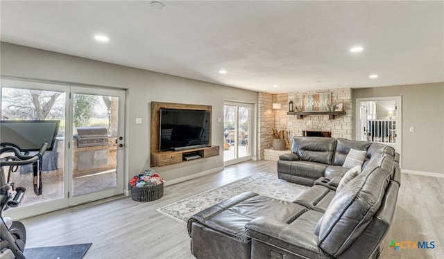 living room with a stone fireplace, light wood-type flooring, and a wealth of natural light