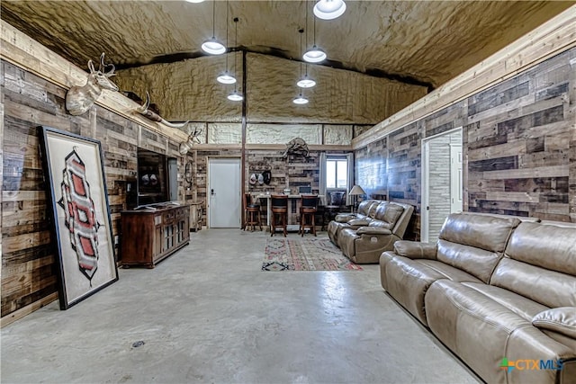 unfurnished living room with high vaulted ceiling, concrete floors, and wood walls