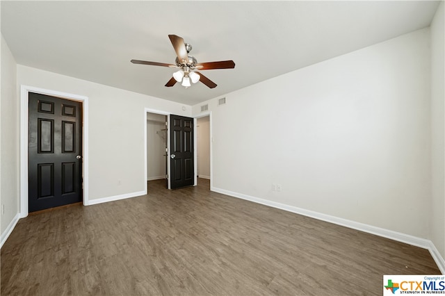 unfurnished bedroom featuring a spacious closet, ceiling fan, dark hardwood / wood-style floors, and a closet