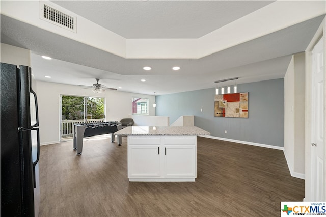 kitchen with black fridge, light stone counters, a center island, dark hardwood / wood-style floors, and white cabinetry