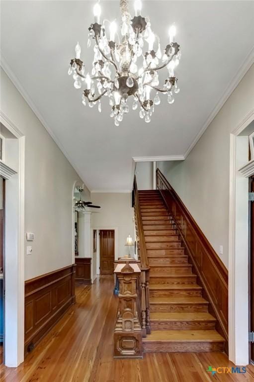 stairway with ceiling fan with notable chandelier, wood-type flooring, and ornamental molding