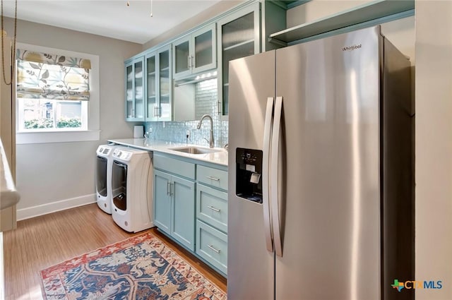 kitchen with sink, stainless steel fridge with ice dispenser, independent washer and dryer, backsplash, and light wood-type flooring