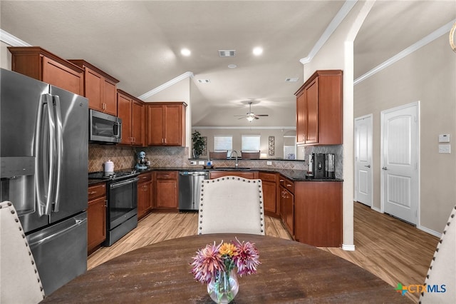 kitchen featuring stainless steel appliances, lofted ceiling, ornamental molding, backsplash, and light wood-type flooring