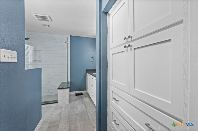 4007 Austin Ave, Waco, TX 76710 - bathroom with tiled shower, vanity, a textured wall, and wood finished floors