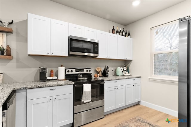 kitchen with light stone countertops, light wood-type flooring, white cabinetry, and appliances with stainless steel finishes