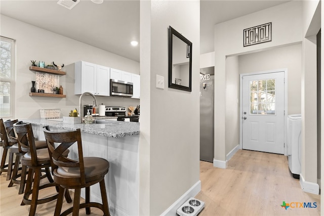 kitchen with white cabinetry, light stone counters, a kitchen bar, appliances with stainless steel finishes, and light wood-type flooring