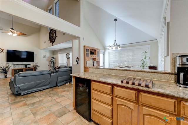 kitchen with high vaulted ceiling, ceiling fan with notable chandelier, wine cooler, decorative light fixtures, and light stone counters