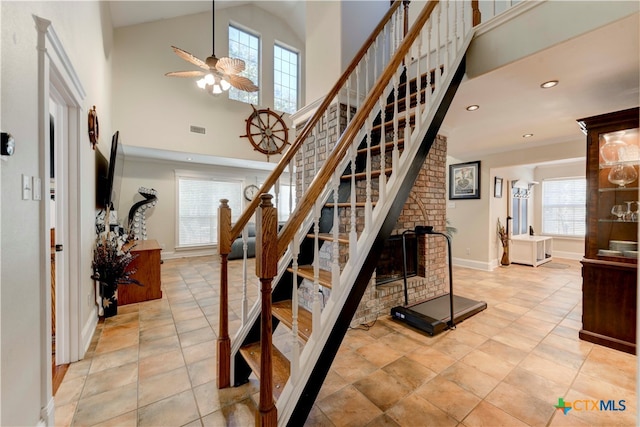 stairs featuring tile patterned floors, ceiling fan, a fireplace, and high vaulted ceiling