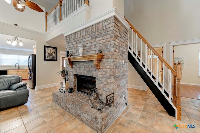 living room with a towering ceiling, ceiling fan, crown molding, sink, and a fireplace