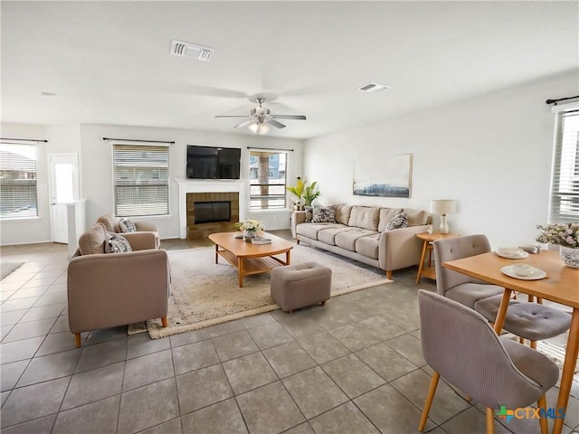 tiled living room with ceiling fan, a tile fireplace, and a wealth of natural light