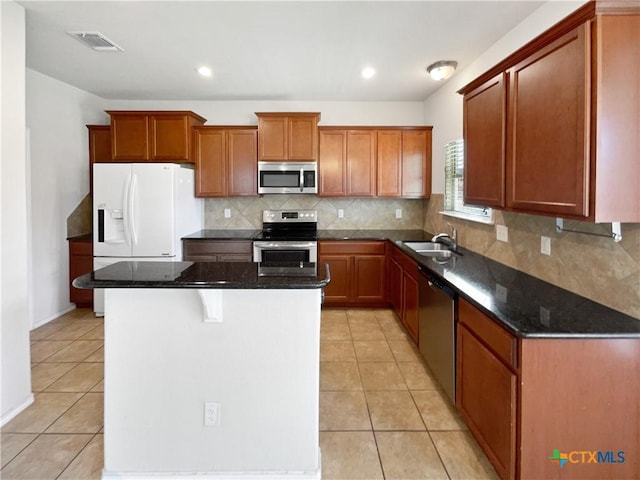 kitchen featuring dark stone countertops, a kitchen island, light tile patterned floors, and appliances with stainless steel finishes