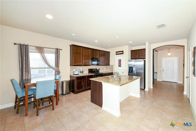 kitchen with sink, light stone counters, black appliances, a center island with sink, and backsplash