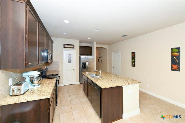 kitchen featuring sink, light stone counters, black appliances, a center island with sink, and decorative backsplash