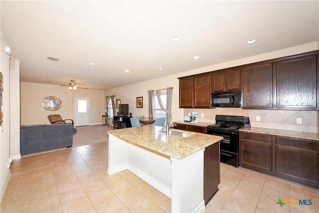 kitchen with tasteful backsplash, sink, light stone counters, black appliances, and a center island with sink