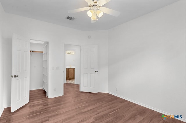 unfurnished bedroom with a walk in closet, a closet, ceiling fan, and dark wood-type flooring