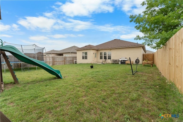rear view of property with a lawn, a trampoline, and a fenced backyard
