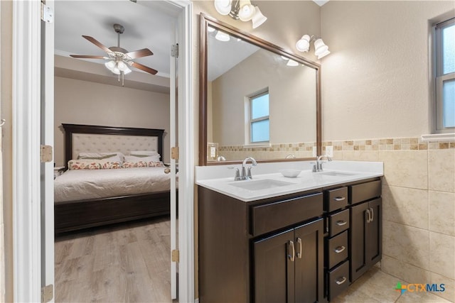 ensuite bathroom featuring connected bathroom, ceiling fan, a sink, double vanity, and tile walls