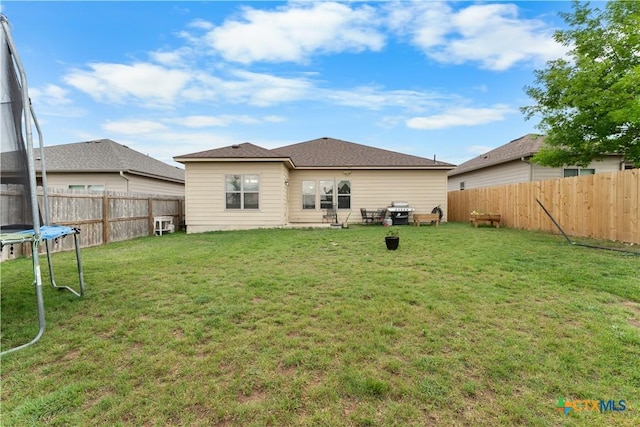 rear view of house featuring a fenced backyard, a trampoline, and a yard